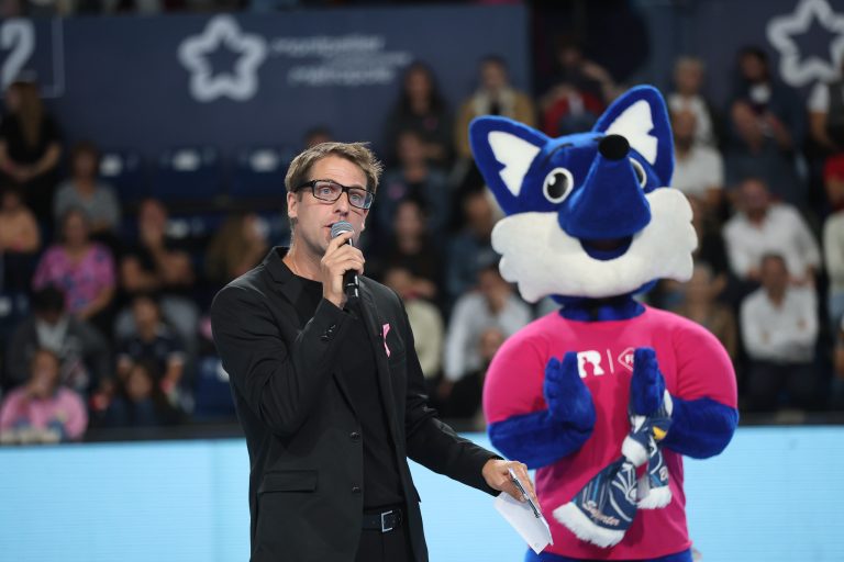 Homme avec micro et mascotte bleu en arrière-plan.