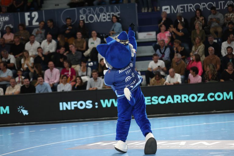 Mascotte bleue saluant le public lors d'un match.