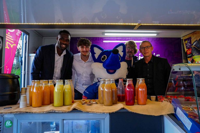 Cinq hommes souriants derrière un stand de jus.
