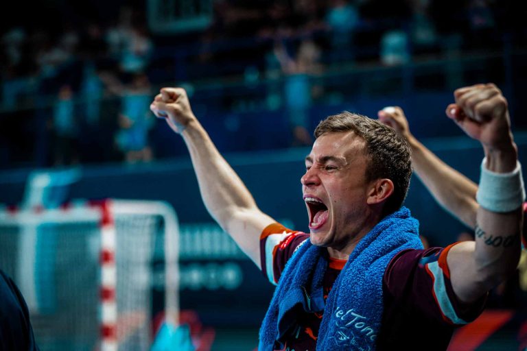 Joueur de handball célébrant une victoire, bras levés.