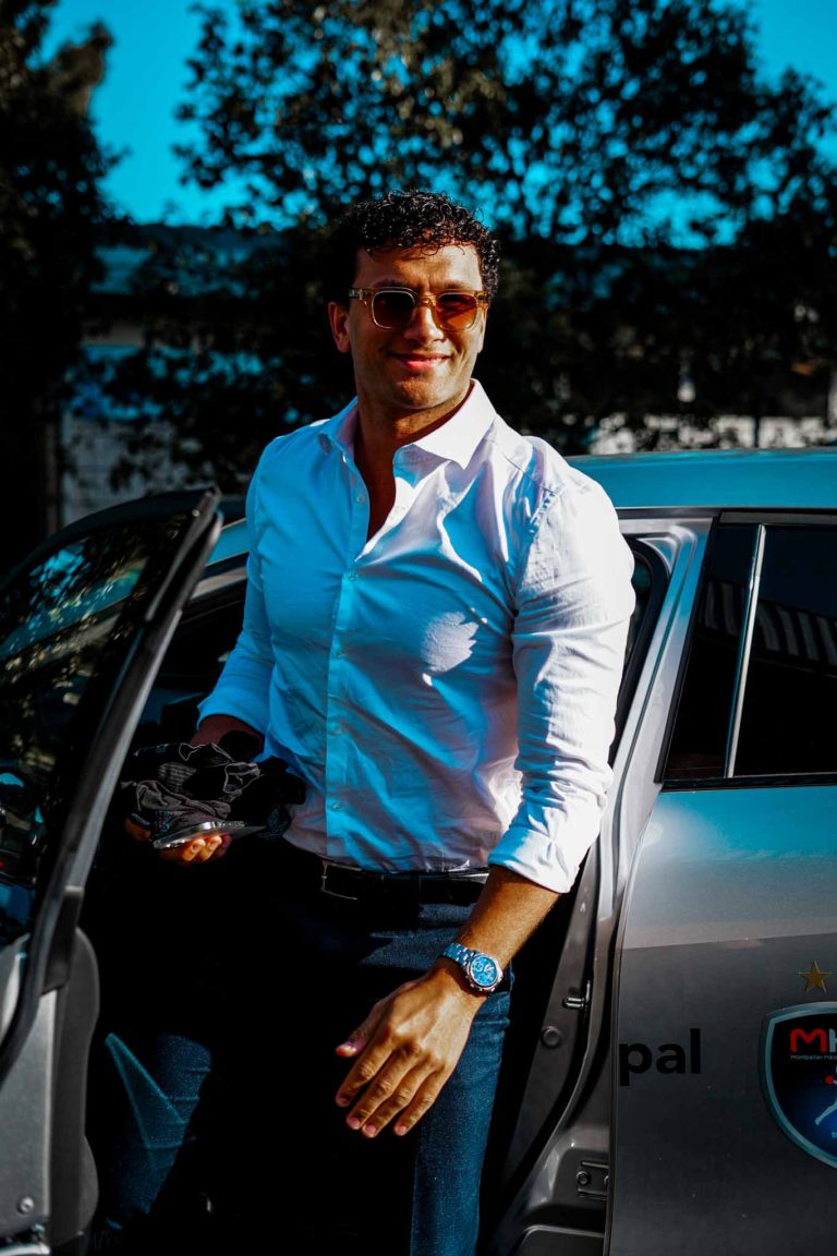 Homme souriant debout à côté d'une voiture.