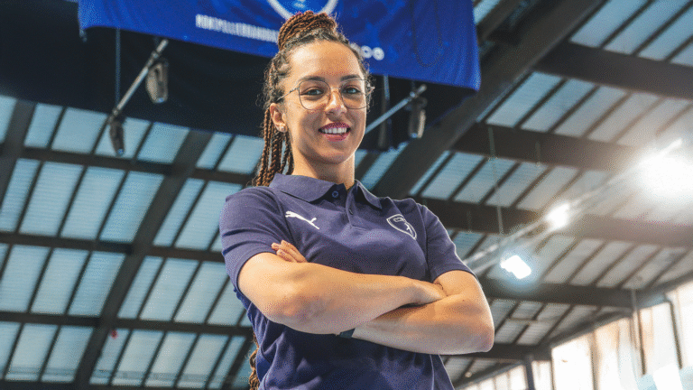 Femme souriante avec des lunettes et polo bleu.