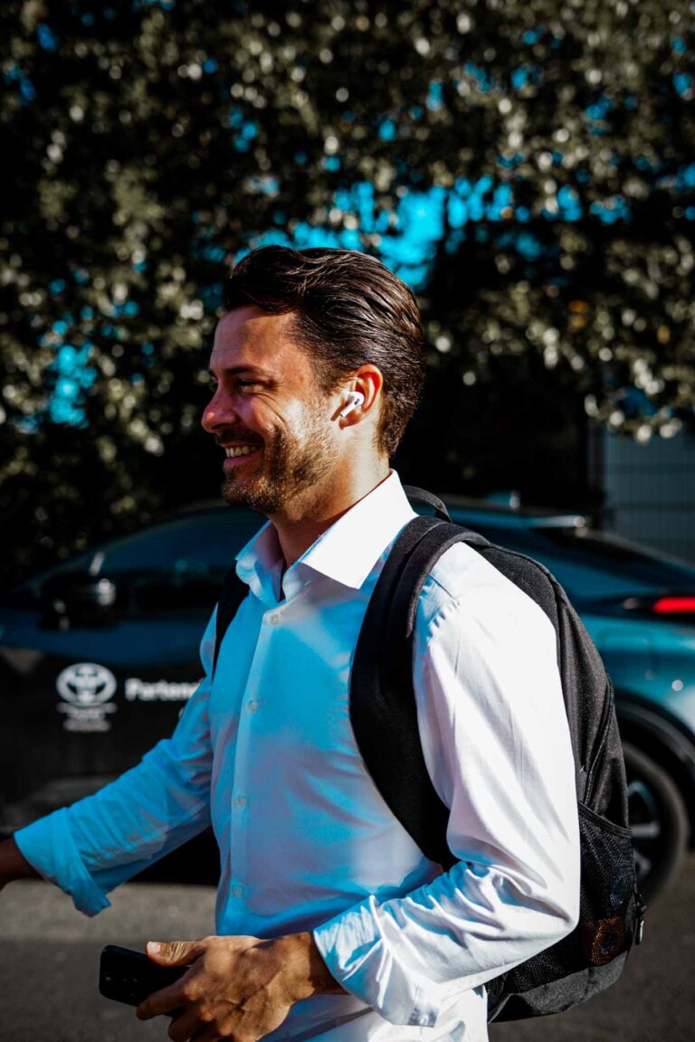 Homme souriant portant un sac à dos et des écouteurs.