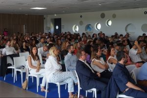 Conférence avec de nombreux participants assis en salle.