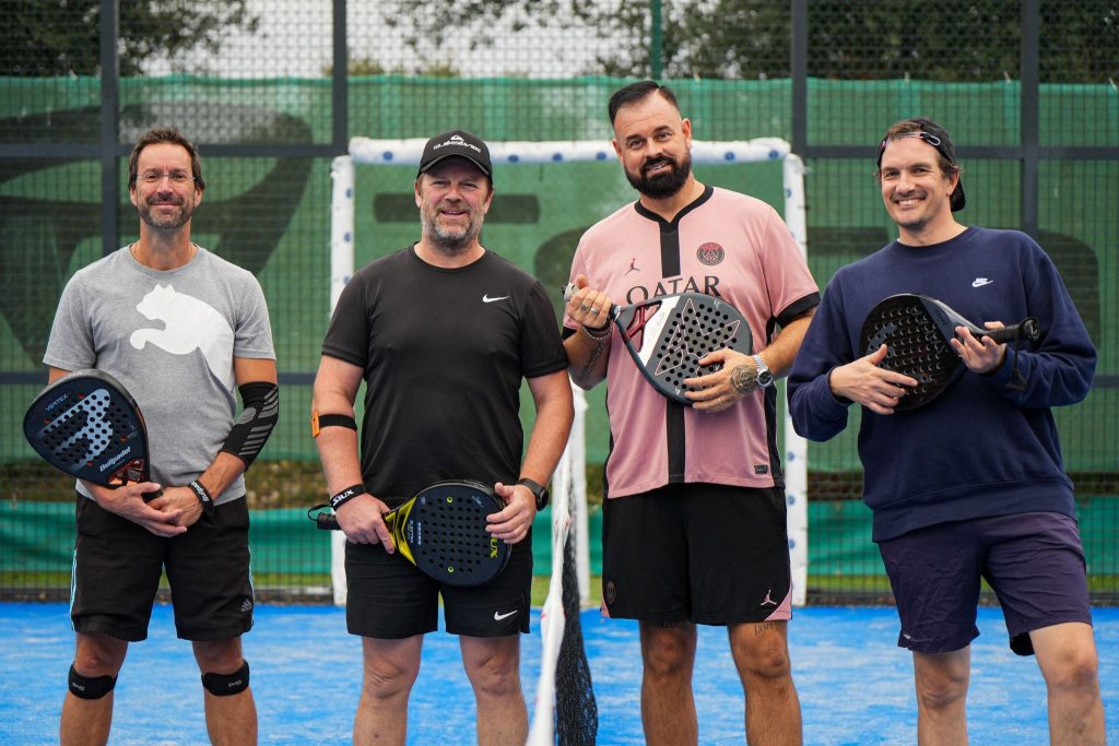 Quatre hommes souriants tenant des raquettes de padel.