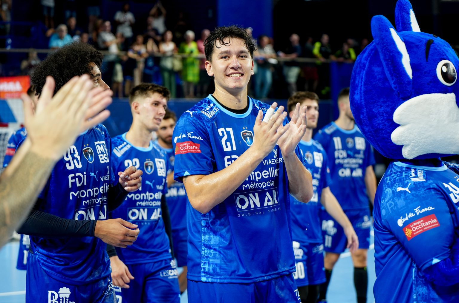 Joueurs de handball applaudissent avec mascotte.
