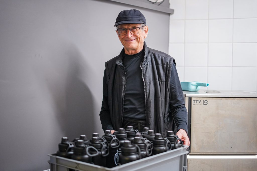 Homme portant un bac de bouteilles noires.