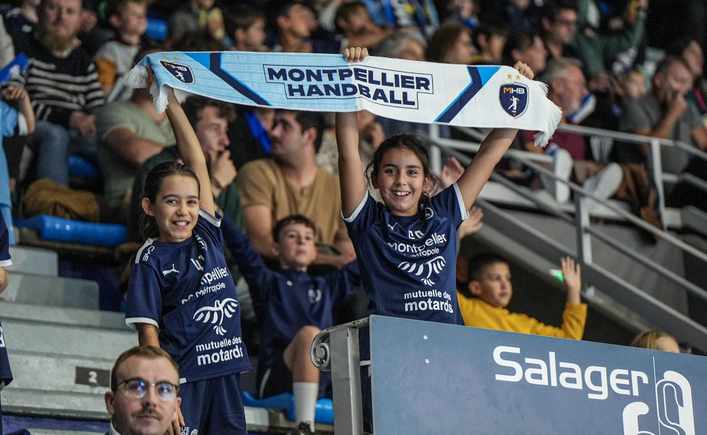 Jeunes supporters avec écharpe Montpellier Handball, tribune sportive.