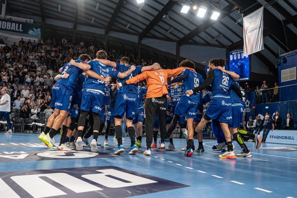 Équipe de handball célèbre en cercle sur le terrain.